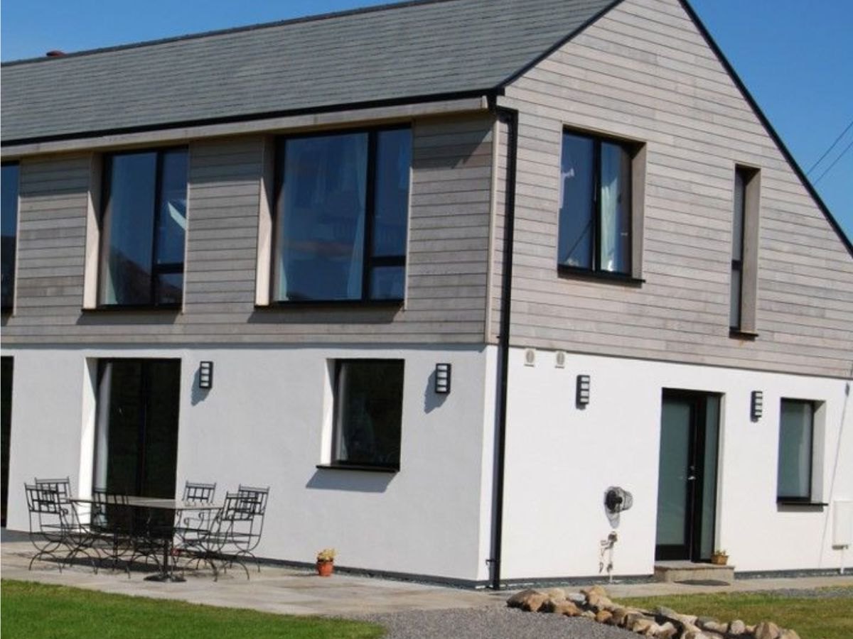 Maison à étage en bardage bois gris clair sur un rez-de-chaussée enduit blanc, baies noires.
