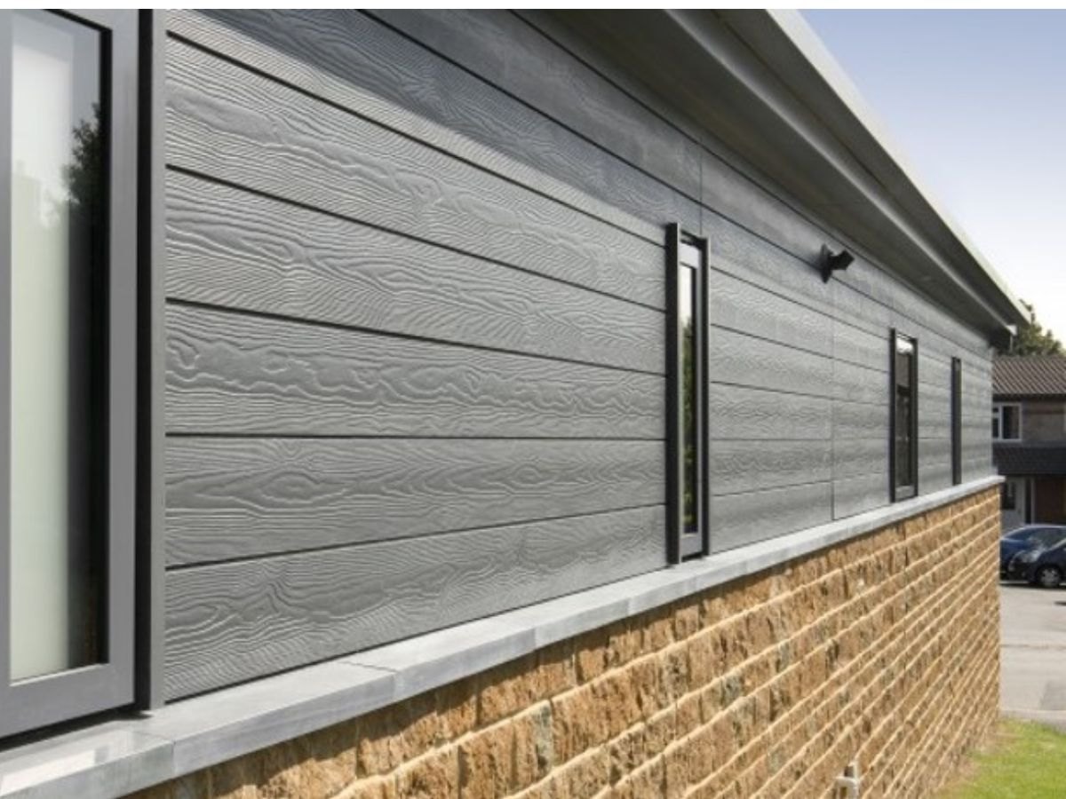 Bardage gris à faux bois au-dessus d'un soubassement en pierre claire, fenêtre noire.