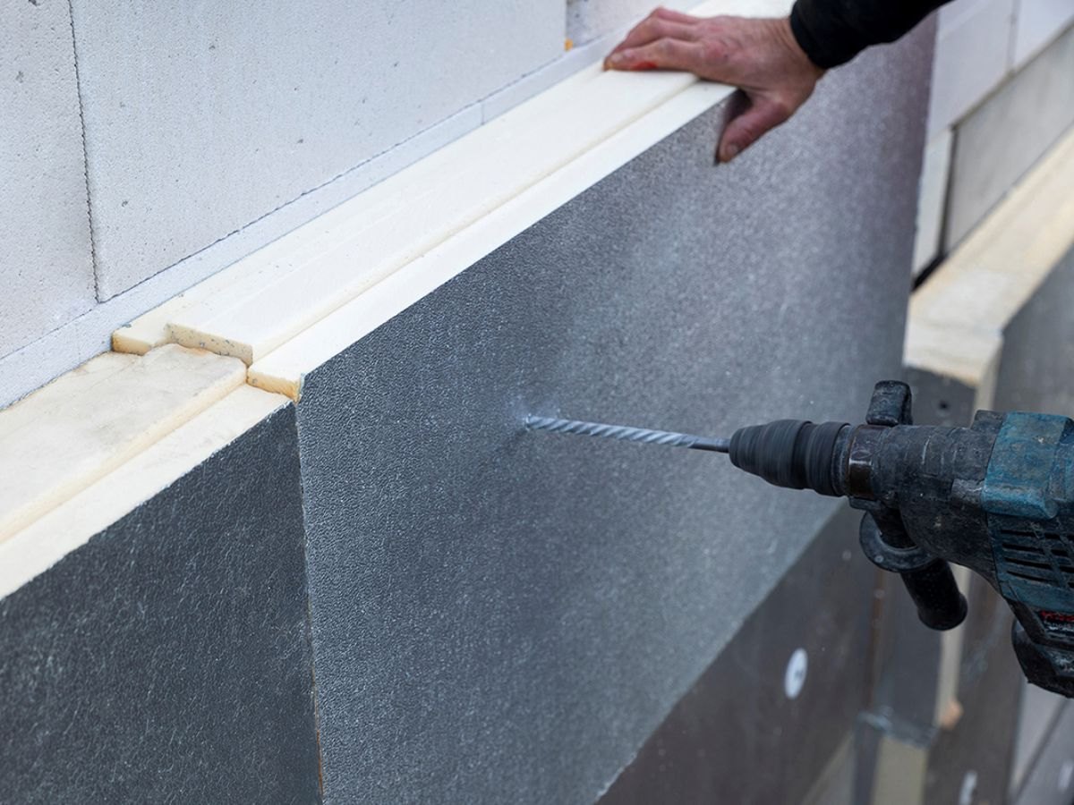 Main et perforateur en train de cheviller un panneau d'isolant gris.