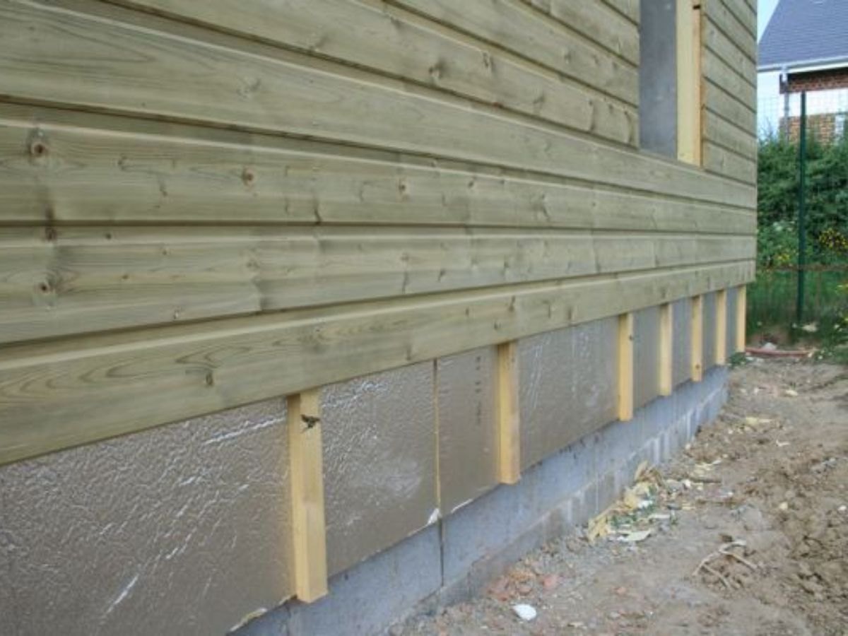 Pied de mur : bardage bois clair au-dessus, isolant argenté entre montants, soubassement béton.
