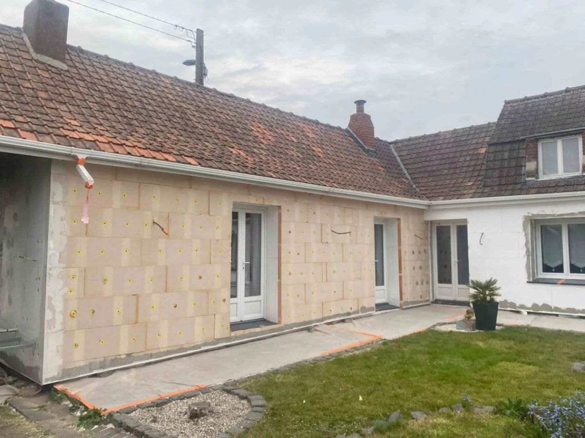 Plaques d'isolant beige chevillées sur une extension, portes blanches, bâche au sol.
