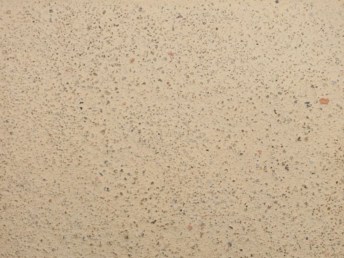 Crépi beige sablé garni de granulats gris et bruns, texture grossière typique d'un enduit chaux minéral.