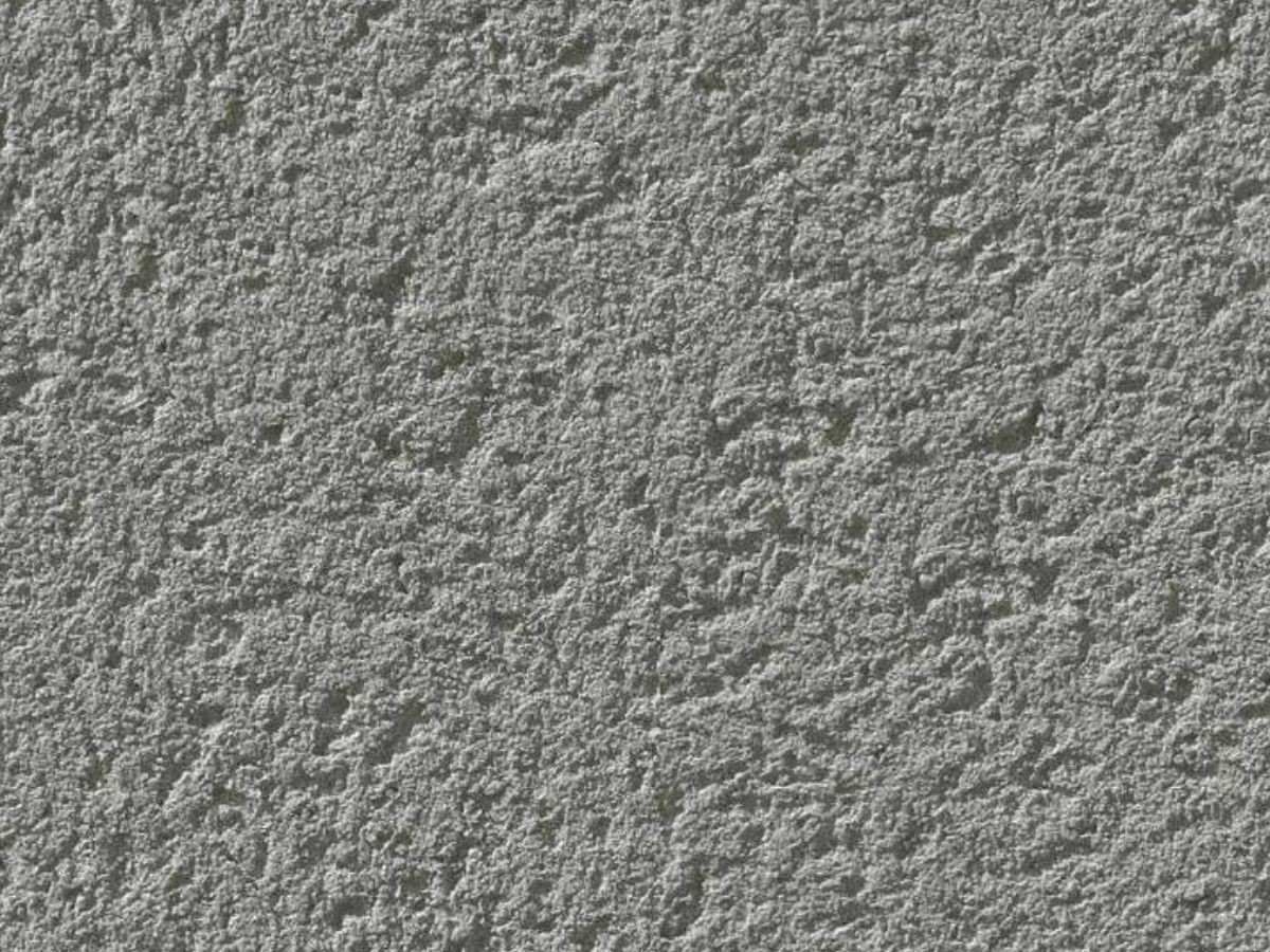 Texture rapprochée d'un crépi monocouche gris moyen, grain grossier, aspérités irrégulières et finition minérale rugueuse.